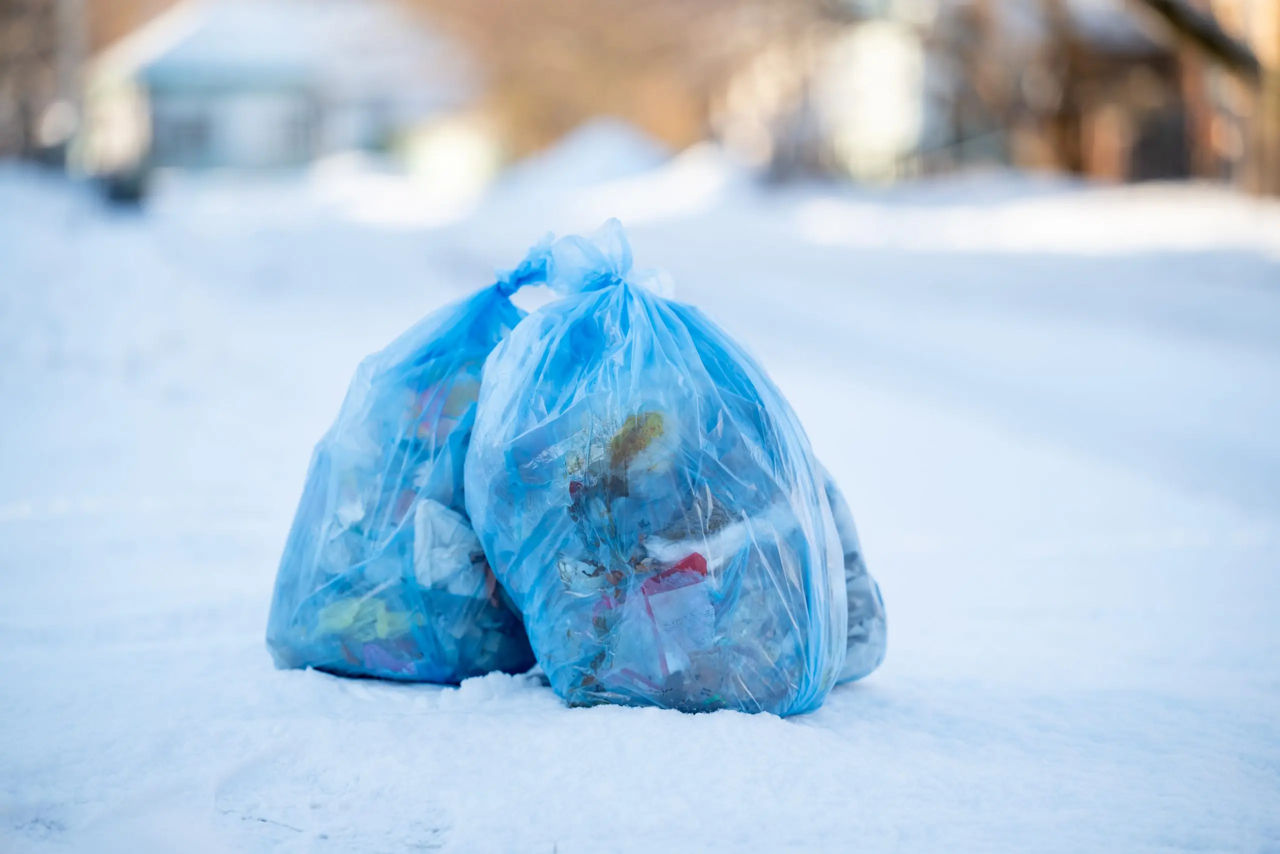 Blue recycling bags on snow covered ground on sunny day in winter.