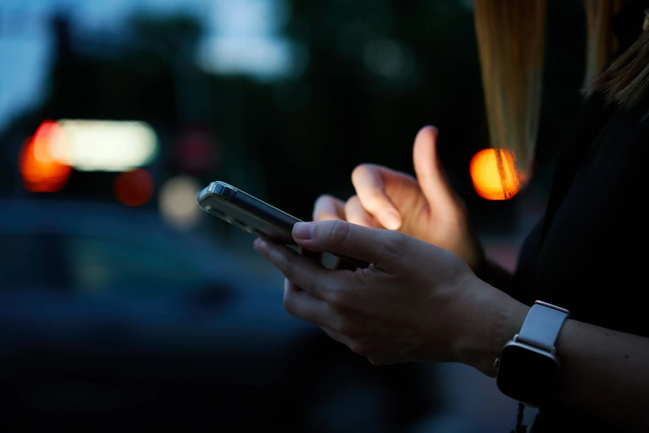 Close up shot of woman using smartphone on city street with bokeh lights at night. Mobile phone in female hands outdoors