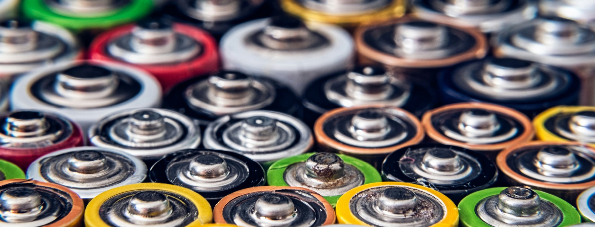 disposable batteries stacked together showing the tops of batteries with various colour casings