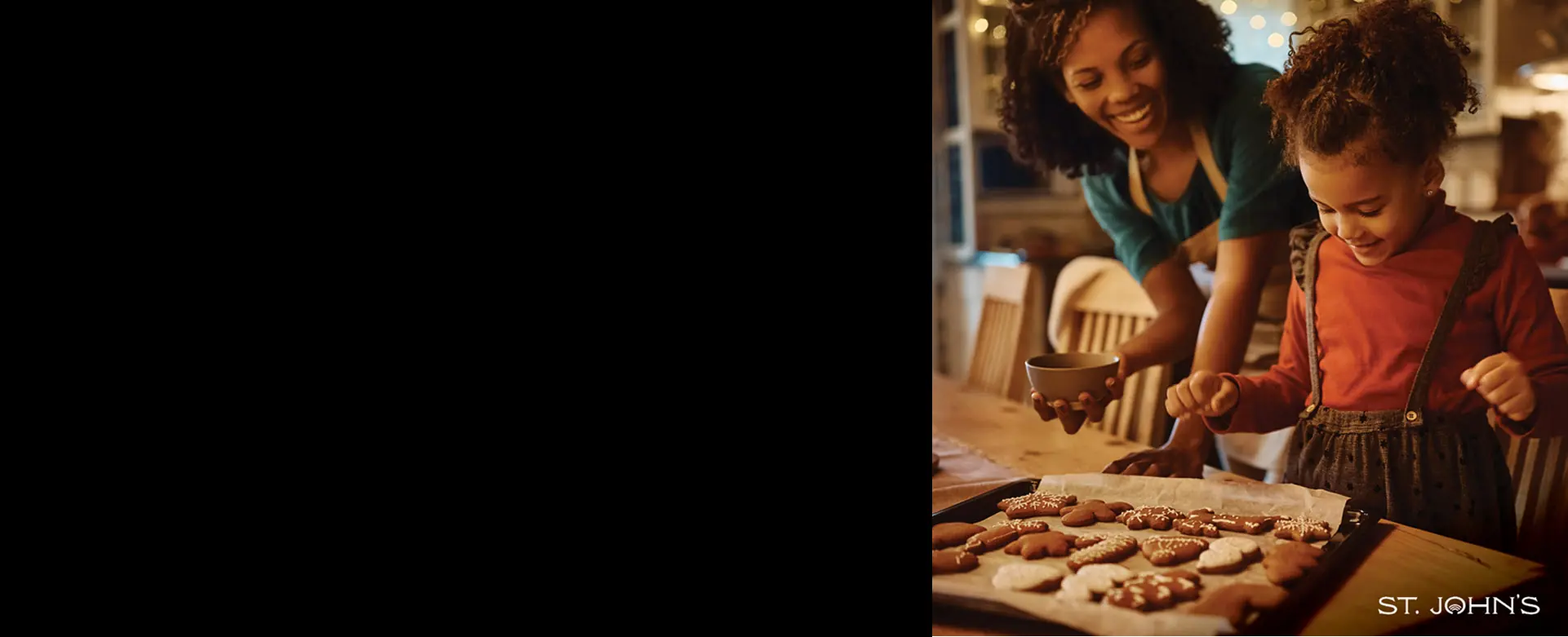 female adult and female child smiling as they decorate gingerbread cookies on a wooden kitchen table.